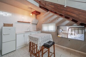 Uma cozinha compacta com geladeira, pia e banquetas de madeira.
