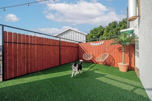 Un patio trasero cercado con césped artificial, una valla de madera y una palmera en maceta.
