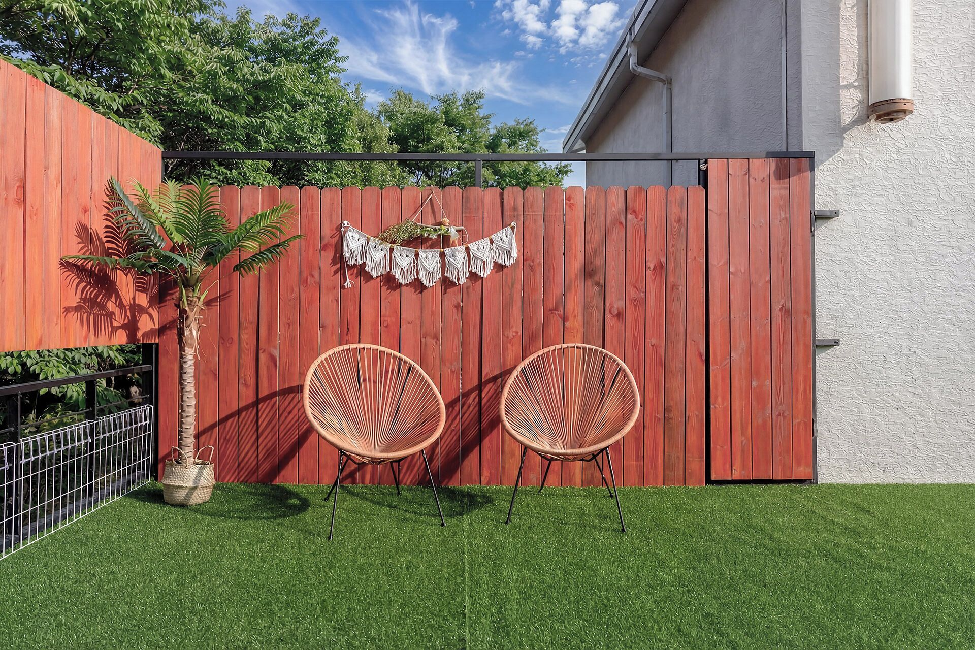 Une clôture en bois rouge, avec deux chaises en osier et une plante sur une pelouse verdoyante.