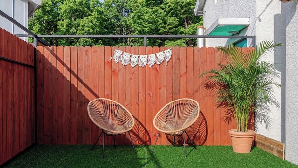A fenced outdoor area with artificial grass, two wicker chairs, and a potted plant.