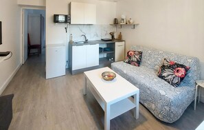 A compact living space with a kitchenette, a sofa with floral cushions, and a white coffee table.