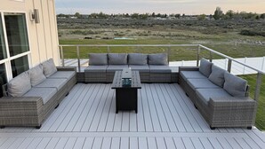 Eine Terrasse mit einer grauen Eckcouch und einem kleinen Tisch, mit Blick auf eine grüne Landschaft.