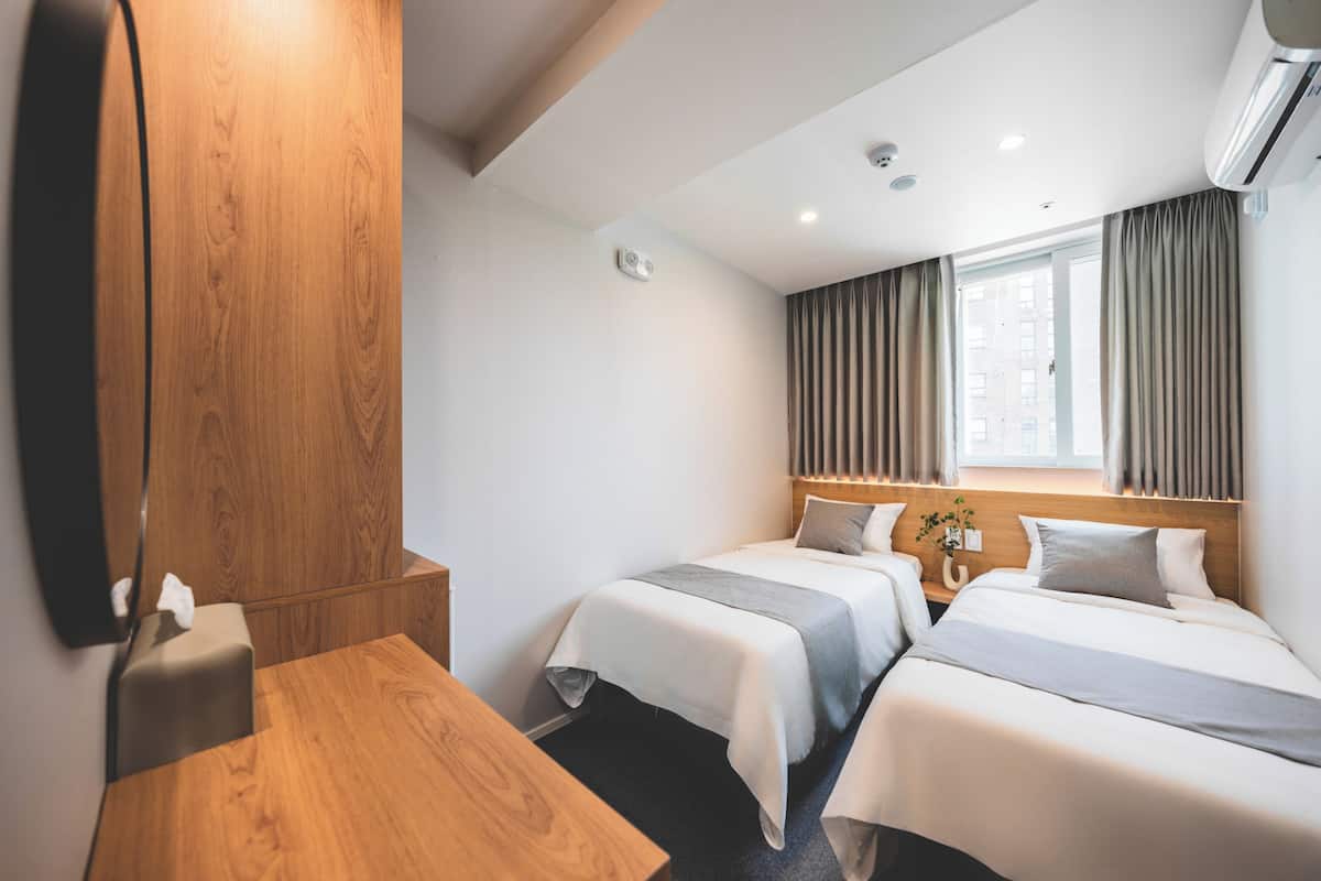 Habitación de hotel con dos camas, un escritorio de madera, un espejo y una ventana con cortinas.