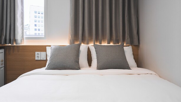 Ein Hotelzimmer mit Bett, Vorhängen, Nachttisch und einer Steckdose.