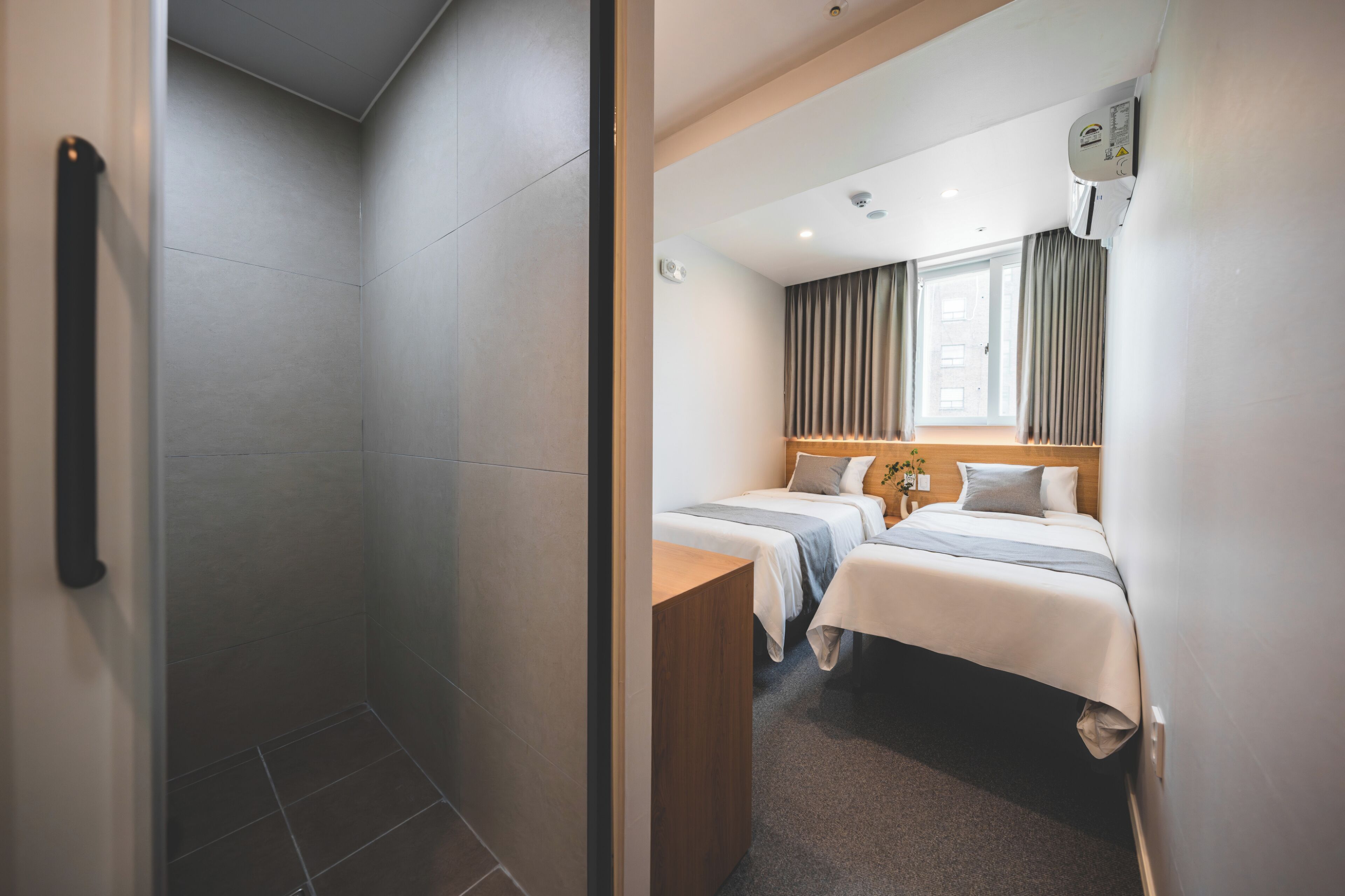Hotelkamer met douche, twee bedden, een houten bureau en een raam met gordijnen.