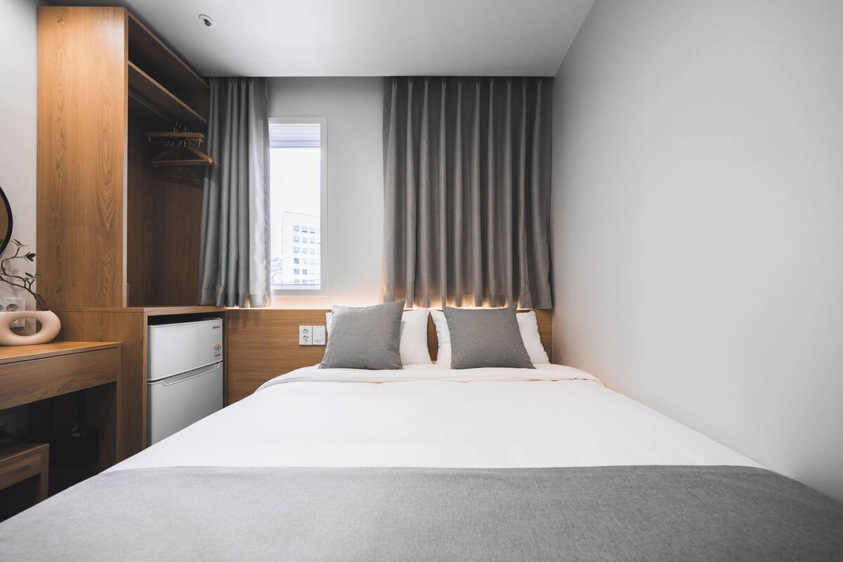 Un dormitorio con cama, armario, escritorio y ventana.