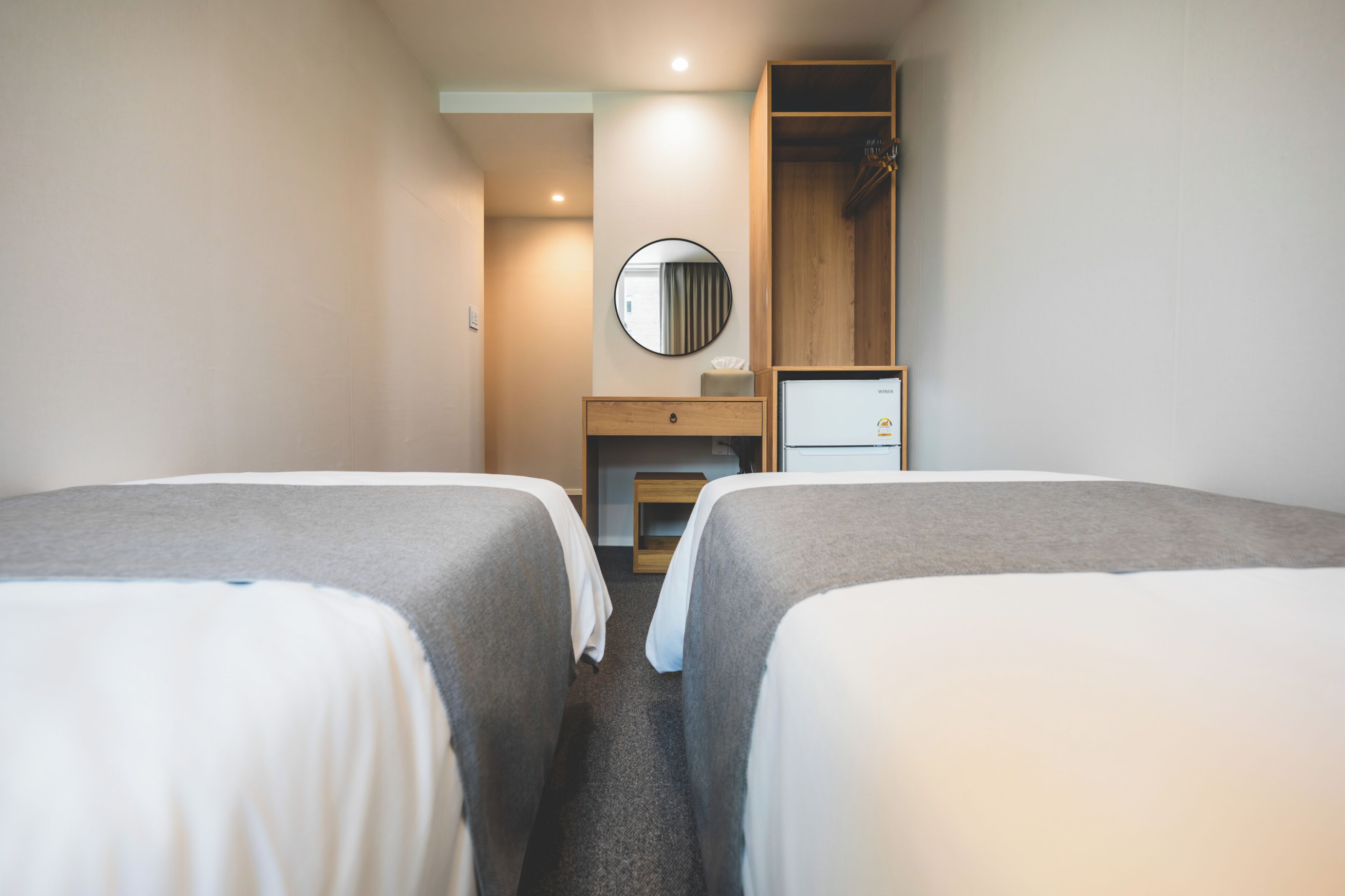 Quarto de hotel com duas camas, um guarda-roupa de madeira, um espelho e uma escrivaninha com um computador.