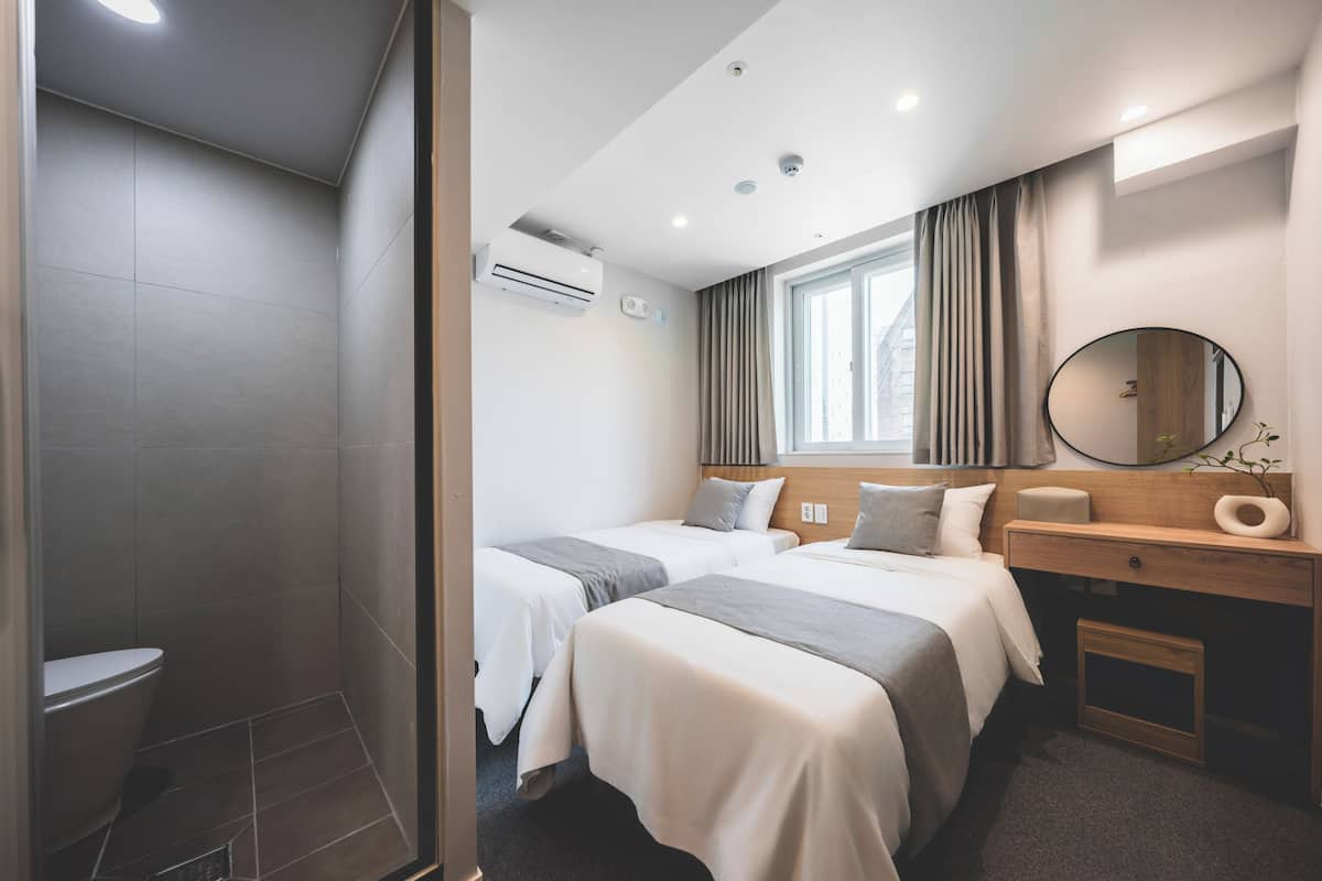 Une chambre dâhĂŽtel avec deux lits, une douche, une fenĂȘtre avec des rideaux, un bureau en bois et un miroir.