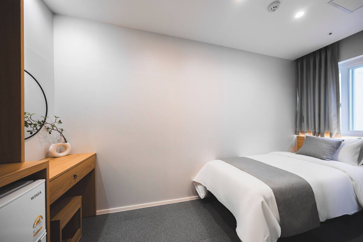 Habitación de hotel con cama, escritorio con computadora, planta y ventana con cortinas.