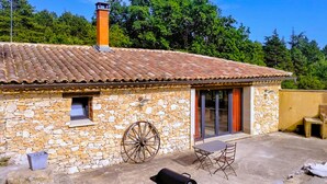 A stone building with a tiled roof, a chimney, a large wheel, and a patio with a table and chairs. - Pet friendly home in Monieux (Monieux)