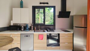 A modern kitchen with a dishwasher, oven, and refrigerator. There is a window with a view of greenery outside. - Pet friendly home in Monieux (Monieux)