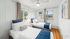 Habitación de hotel con dos camas, ventilador de techo y ventanas amplias.