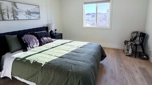 Et soveværelse med en stor seng, et natbord, en lampe, en stol, et vindue og en loftlampe.