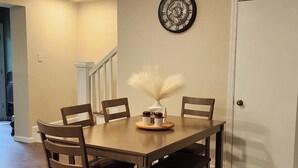 Un comedor con una mesa de madera, seis sillas, un reloj decorativo y un jarrón con plumas de pampa.