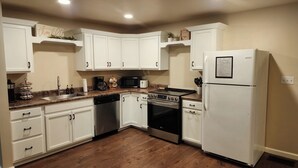 Una cocina con armarios blancos, lavavajillas de acero inoxidable, horno, microondas, cafetera y refrigerador blanco.