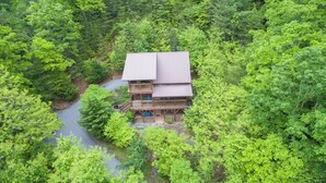 Een houten chalet met twee verdiepingen, omgeven door dicht bos, met een geplaveid pad er naartoe.