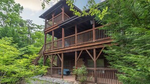 Een houten vakantiehuis met meerdere verdiepingen en een balkon, omgeven door dicht bos.
