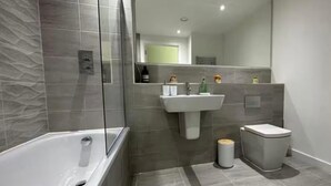 A modern bathroom with a freestanding bathtub, a pedestal sink, and a toilet. - Modern 1-Bed Penthouse — Steps from Old Trafford (Stretford)