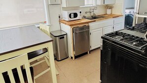 Cocina compacta con mesa de madera, un lavamanos, microondas, refrigerador pequeño y estufa negra.