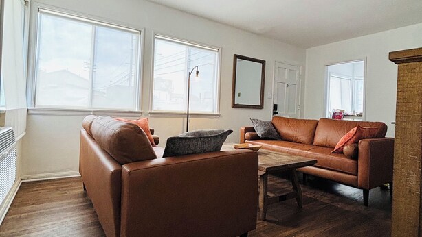 Un salón amplio con dos sofás de cuero, una mesa de centro de madera y grandes ventanas que dejan entrar mucha luz natural.