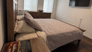 Un dormitorio con cama, un banco de madera, un ventilador de techo y dos ventanas.
