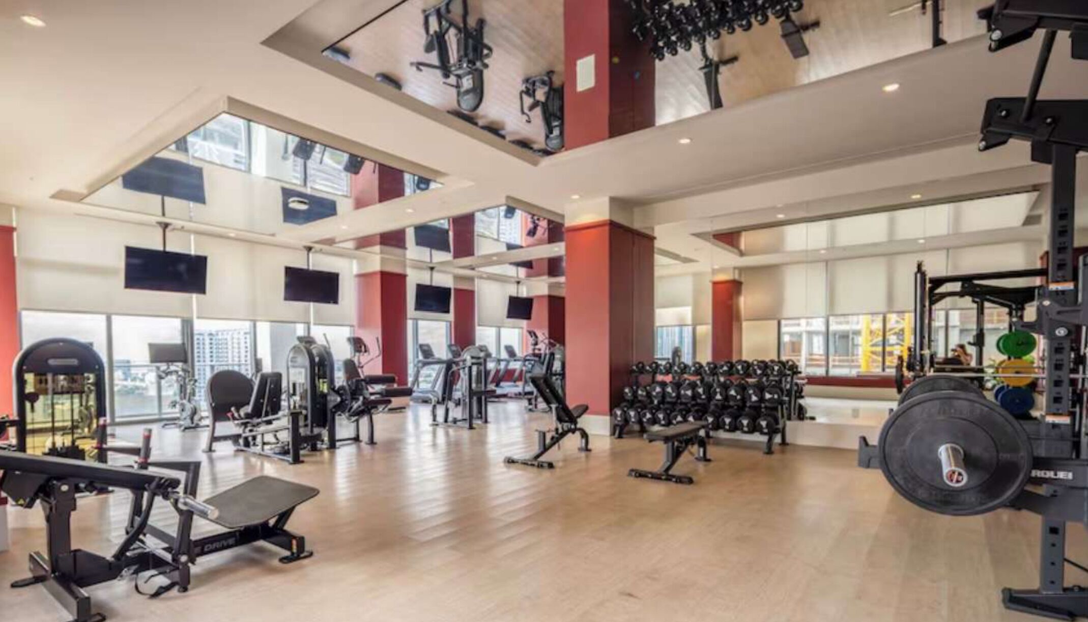 A spacious gym with various exercise equipment, large windows, and a high ceiling.