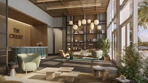 Un intérieur moderne comprenant un comptoir d’accueil portant l’inscription « THE CROSBY », un espace détente avec des canapés et une table basse, ainsi qu’une bibliothèque remplie de livres et d’objets décoratifs.