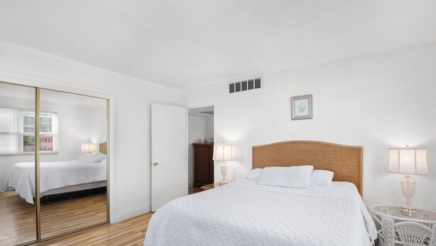 Una camera da letto con un grande letto, una testiera in legno, un comodino con una lampada, uno specchio e un armadio.