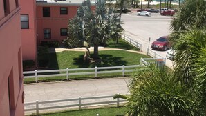 Un balcone con vista sulla spiaggia, palme e un'area di parcheggio con auto.