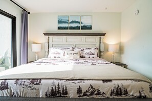 A neatly made bed with a mountain-themed bedspread, two bedside lamps, and a headboard with a decorative panel. - Gatlinburg Mountain Charm, Walk to DTWN, Sleeps 4, Elevator on Premises (Gatlinburg)
