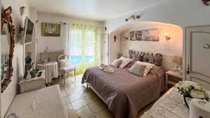 Een slaapkamer met een groot bed, een nachtkastje, een stoel, een bureau, een spiegel en een raam met gordijnen.