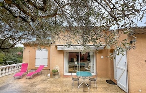 Un patio con dos sillones rosas, una mesa, sillas, una fuente de piedra y una puerta de cristal que da a un espacio interior.