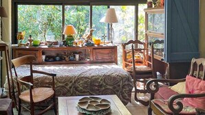 Ein gemütliches Zimmer mit einem Bett, zwei Stühlen, einem Tisch mit Dekoration und einem Fenster mit Blick auf Grünflächen.