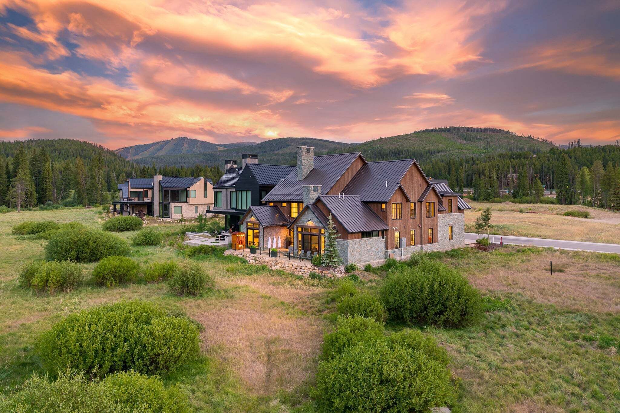 A large, modern house with multiple sections, surrounded by a natural landscape and mountains.