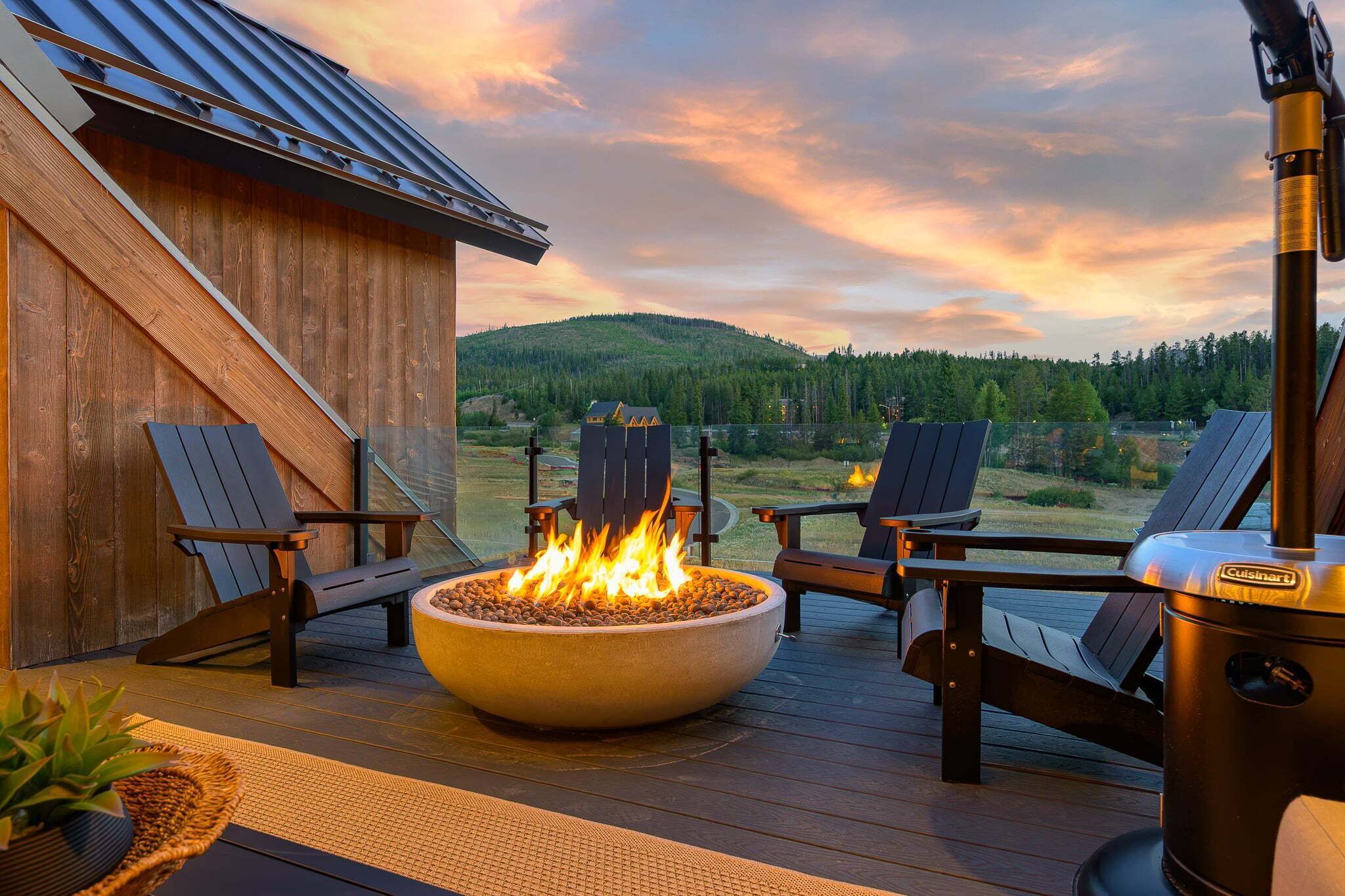 Une terrasse extérieure avec un foyer, deux fauteuils Adirondack et un barbecue.