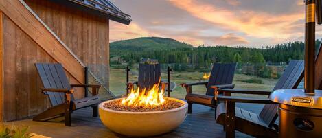 Une terrasse extérieure avec un foyer, deux fauteuils Adirondack et un barbecue.