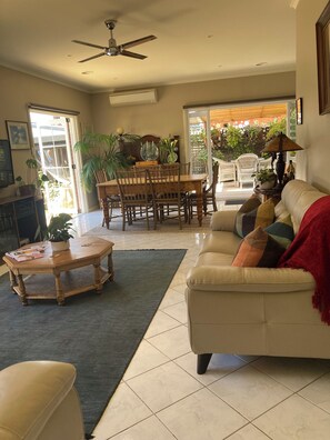 A living room with a sofa, coffee table, dining table, chairs, and a ceiling fan.