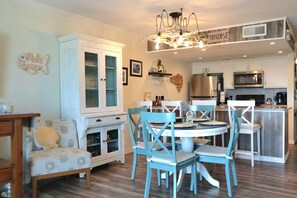 A kitchen with white cabinets, a stainless steel refrigerator, a microwave, and a dining area with blue chairs and a white table. - 3-bedroom town home on the water with a pool, fishing pier, boat ramp!!!! (Rockport)