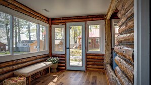 Interior de cabana de tronco com um banco, uma cesta de vime e uma porta que dá para o exterior.