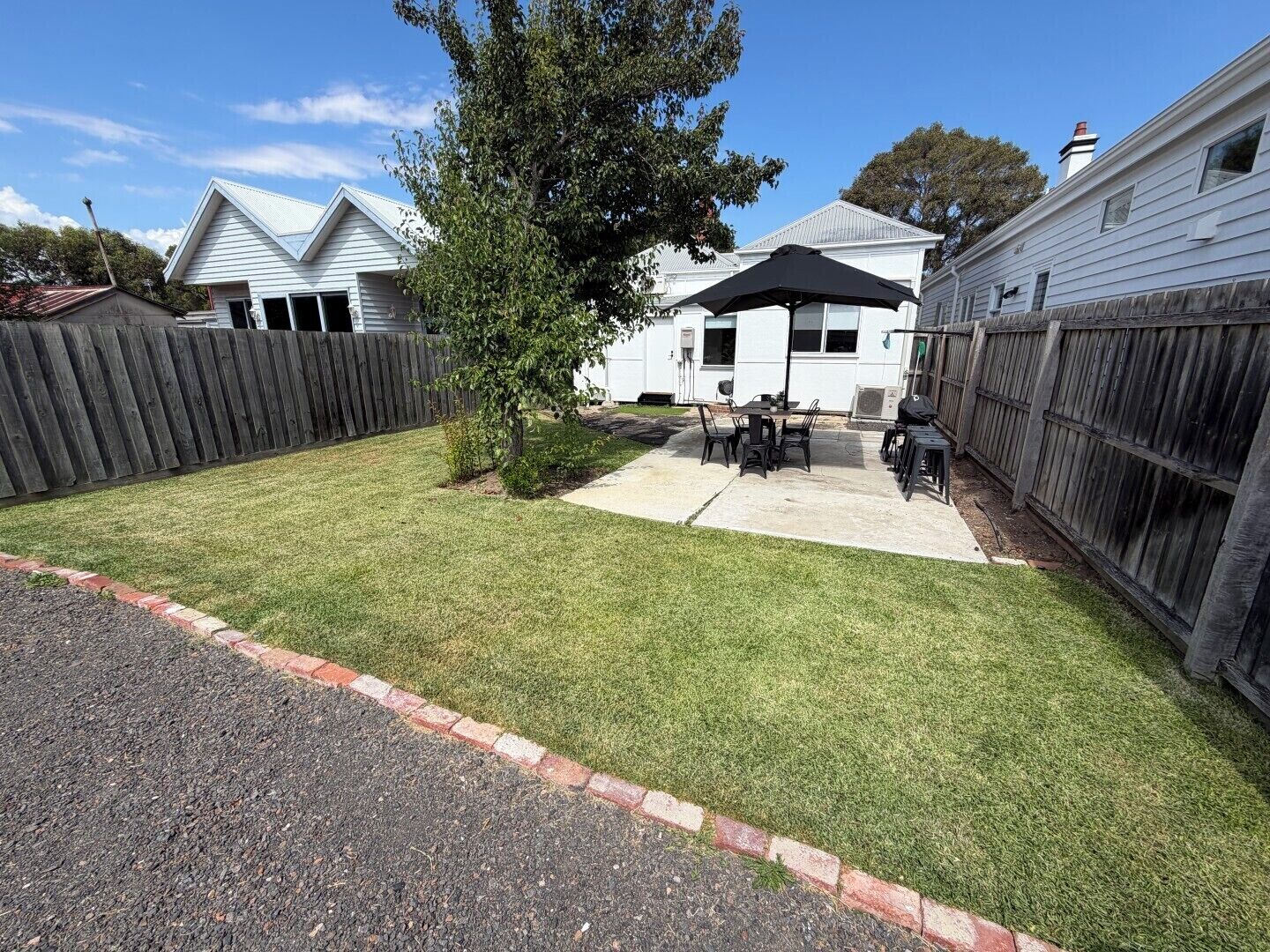 A backyard with a patio, a wooden fence, and a house.
