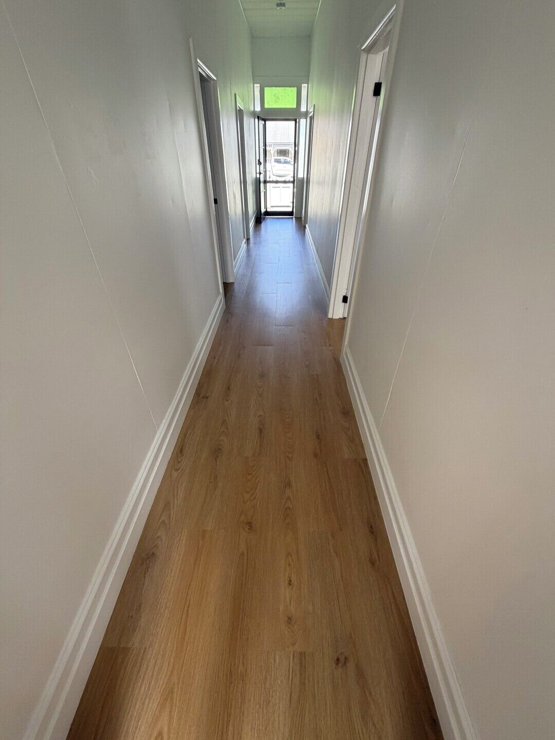 Un long couloir étroit, doté d’un plancher en bois et de murs blancs.