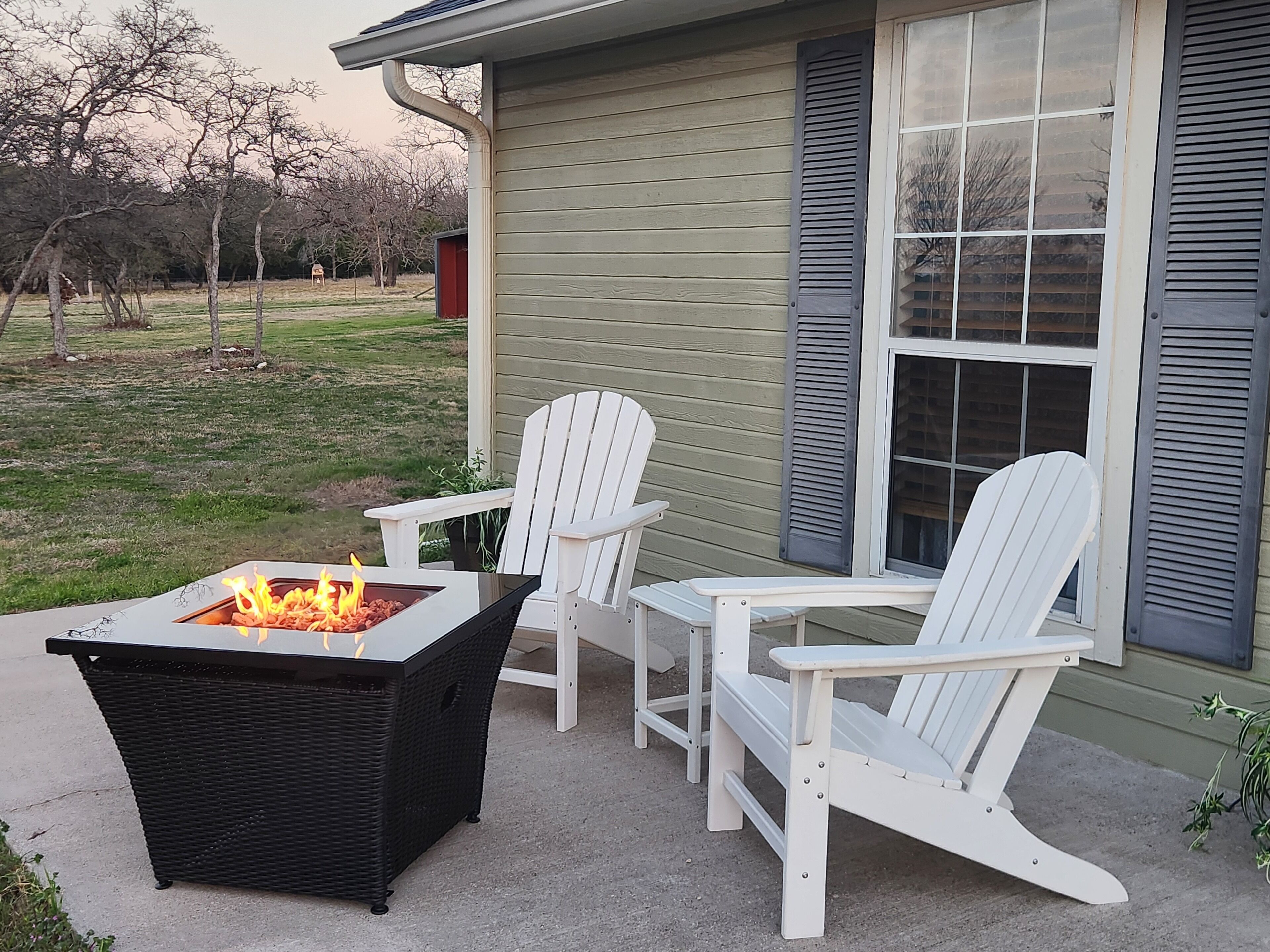 An outdoor seating area with two white Adirondack chairs and a black fire pit table.