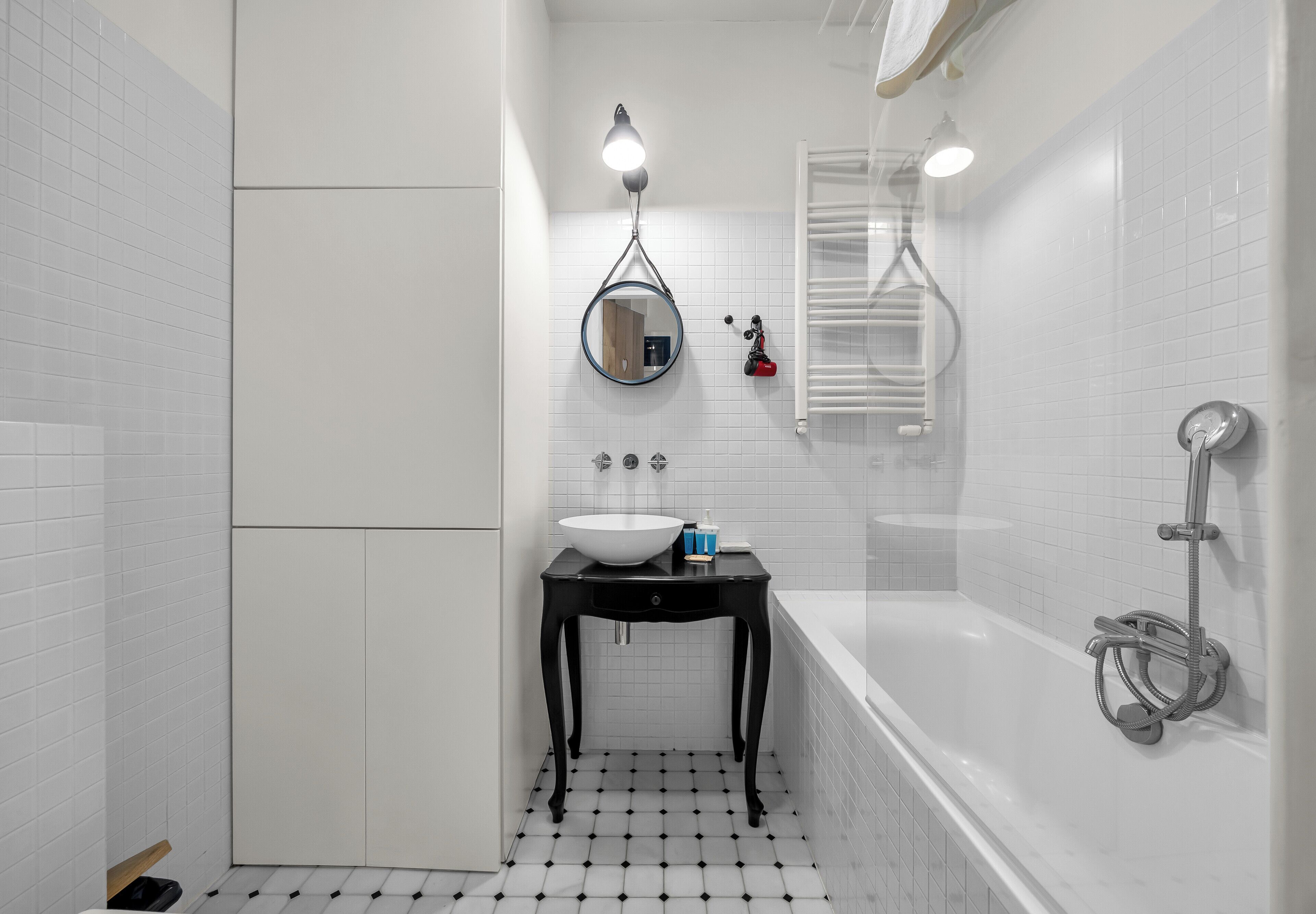 A bathroom with a white tiled floor, a black vanity with a white sink, a mirror, and a bathtub with a showerhead.