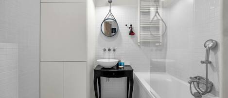 A bathroom with a white tiled floor, a black vanity with a white sink, a mirror, and a bathtub with a showerhead.