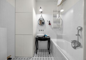 A bathroom with a white tiled floor, a black vanity with a white sink, a mirror, and a bathtub with a showerhead. - Royal Baths Superior Apartment (Warszawa)