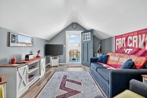 A modern loft bedroom with a large window, a ceiling fan, a TV, a desk, and a cozy seating area with a large rug.