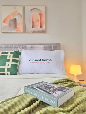A neatly made bed with a Nordic Interiors Homes book, a green blanket, and a white pillow. - Whiz By SanLiving - Studio (Jakarta)