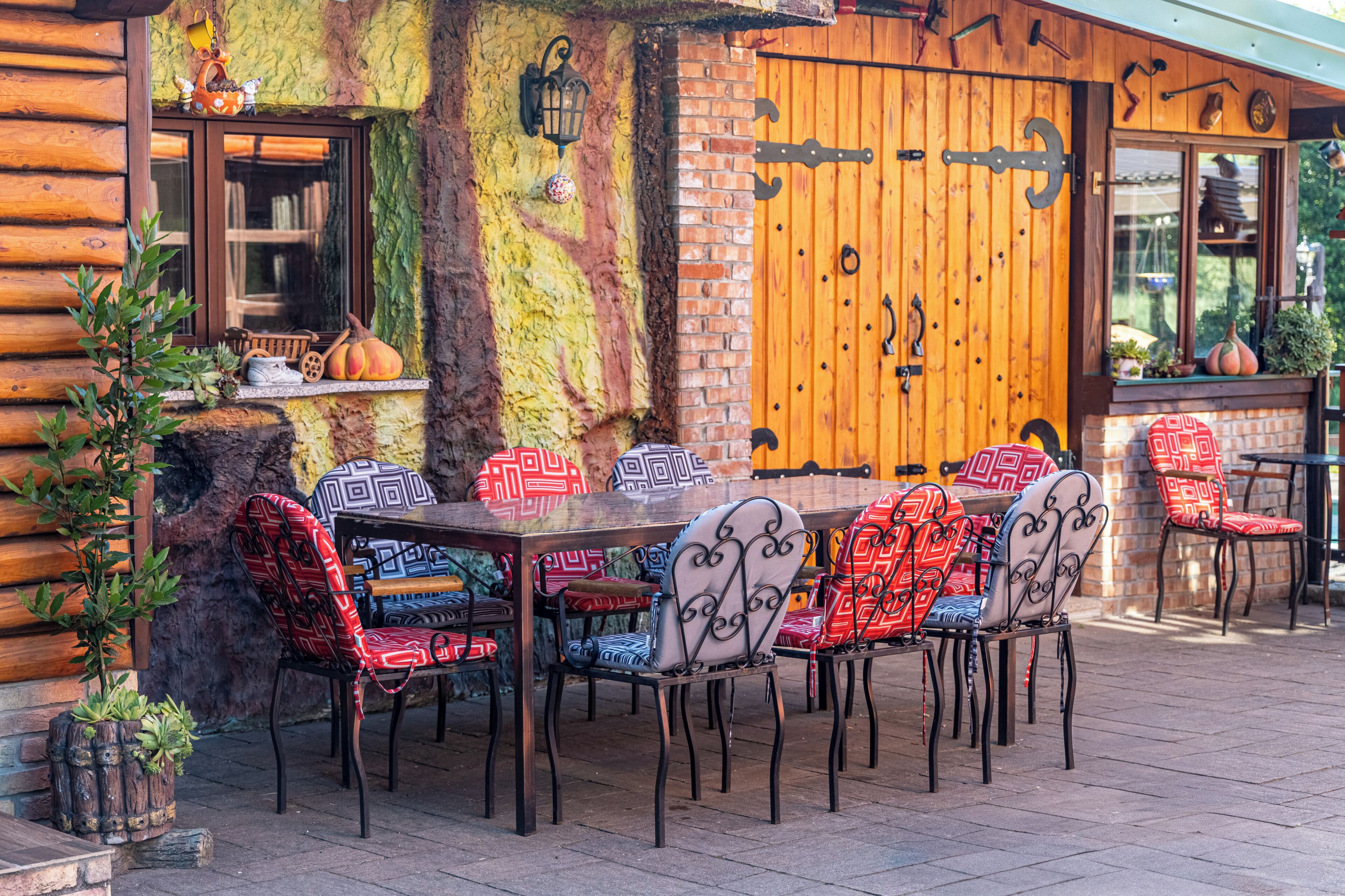 A rustic wooden cabin with a dining area featuring a wooden table and metal chairs with patterned cushions.