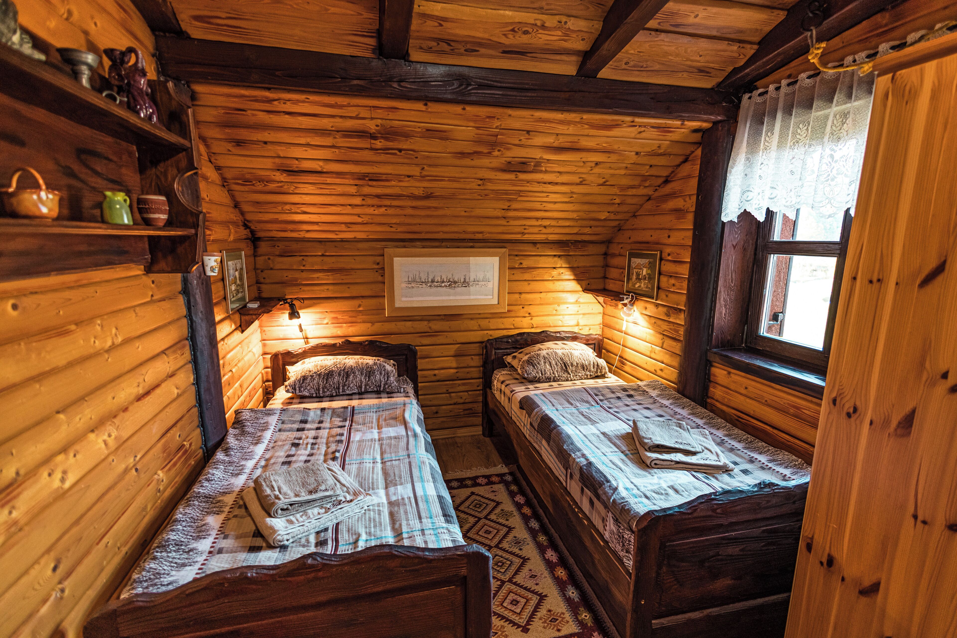 Une cabine avec deux lits en bois, une fenêtre ornée de rideaux en dentelle et une étagère fixée au mur, sur laquelle sont disposés divers objets.