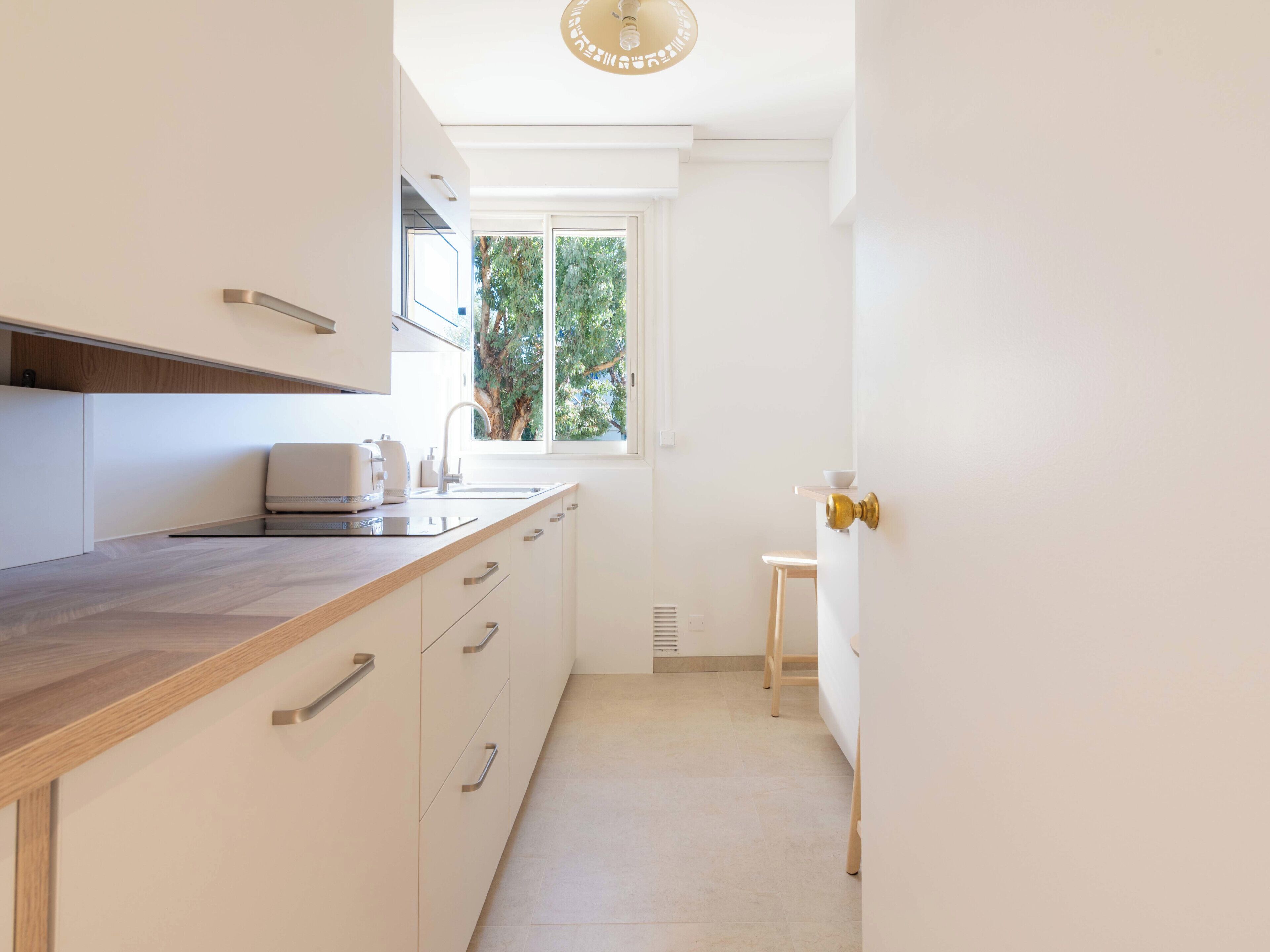 A modern kitchen with a wooden countertop, built-in appliances, and a window providing a view of greenery.